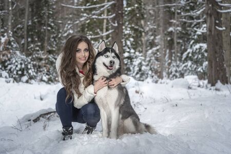 Beautiful girl plays with a dog in a snowy forest.