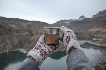 First-person view, on hands with a mug, high in the mountains. Trekking concept. Rest during the ascent.の写真素材