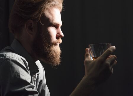 Portrait of a handsome young man with a beard drinking alcohol from a glass.の写真素材