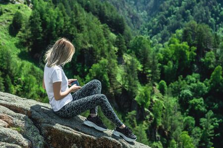 A young woman sits high in the mountains, among the greenery, relaxing on vacation. Climbing to the mountains.の写真素材