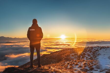 A man stands high in the mountains, at sunset, above the clouds. Conceptual design.