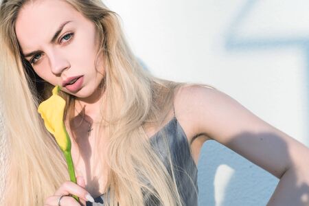 Stylish, beautiful blonde girl with a flower in her hands, against the background of a geometric...