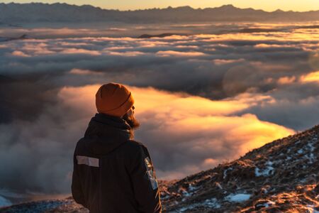 A man stands high in the mountains, at sunset, above the clouds.の写真素材