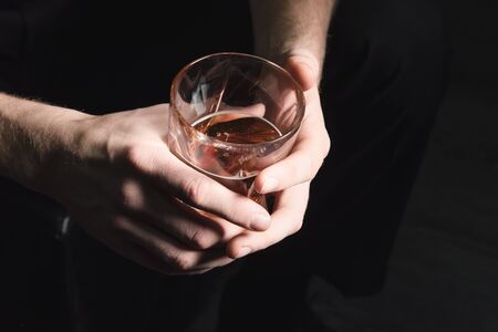 Close-up of the hands of a young man who pours alcohol from a decanter into a glass, on a dark isolated background.の写真素材