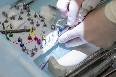Close-up of the hands of a dentist surgeon on implantation, with dental instrument and surgical...