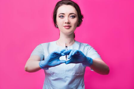 Woman cosmetologist doctor with a syringe in hands on a pink background in the studio. The concept of cosmetology, medicine and beautyの写真素材
