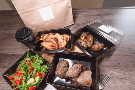 Food delivery. Closeup of boxes with meat and salad on the table. The concept of isolation, finding a home, food delivery and saving timeの写真素材