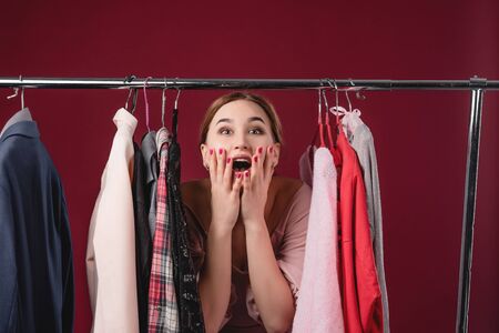 Beautiful girl chooses and tries on clothes on a red background. The concept of choosing and buying clothes, shopaholism and consumerismの写真素材