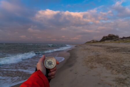 First-person view of a female hand with a compass on a background of a beautiful sea landscape. The...
