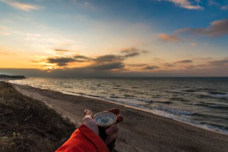 First-person view of a female hand with a compass on a background of a beautiful sea landscape. The...