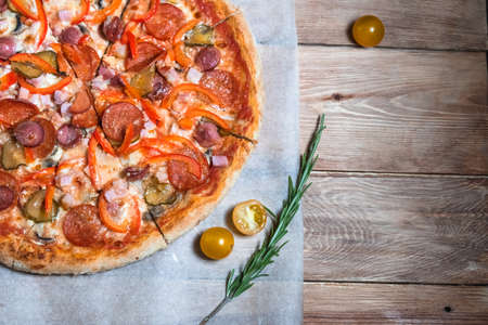Appetizing pizza on a wooden table surrounded by herbs and spices. The concept of delicious food, restaurants and cafesの写真素材