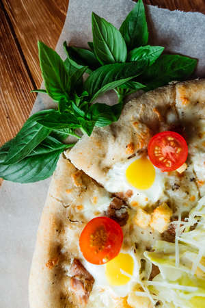 Appetizing pizza on a wooden table surrounded by herbs and spices. The concept of delicious food,...