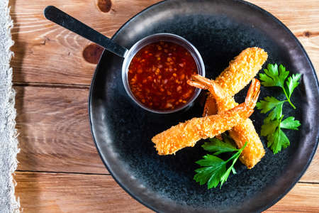 Appetizing fried shrimp on a dark plate stand on a wooden table with sauce and herbs. The concept of food, serving, bars and restaurantsの写真素材