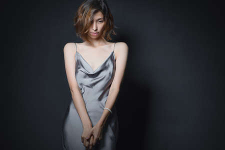 Portrait of a beautiful young girl on a dark background in a gray silk dress. The concept of beauty, youth and naturalnessの写真素材