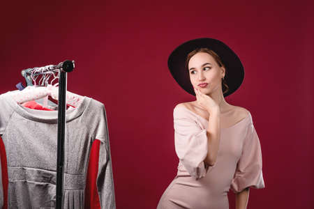 Portrait of a beautiful women in a pink dress and hat on a red background in the studio. Clothing, fitting and beauty conceptの写真素材