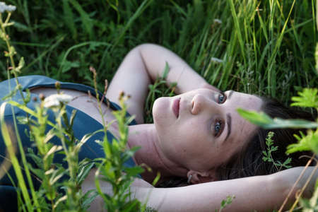 A beautiful blonde woman in a blue long dress lies in a field in flowers. The concept of beauty, free life and naturalnessの写真素材