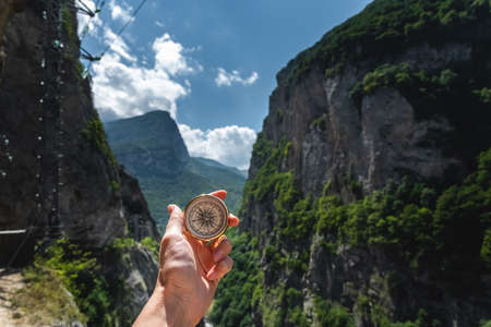 First-person view of a female hand with a compass on a background of a beautiful mountain landscape. The concept of navigating the search for your own path and orientation to the cardinal pointsの写真素材