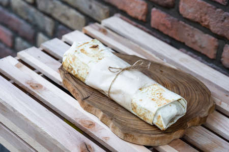 Ready shawarma lies on the board against the background of the wall. Fast food and national street...