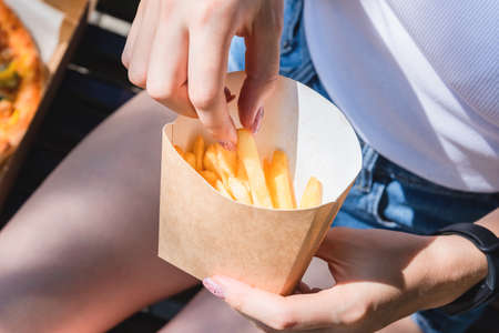 Beautiful, young woman eating pizza and fries in the street. The concept of fast food, food delivery...