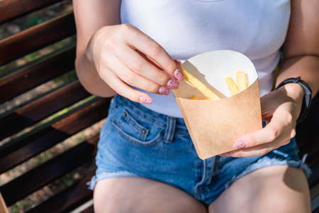 A slender girl holds a cardboard box with fried potatoes in her hands, close-up. Street food conceptの写真素材