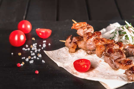 Appetizing pieces of meat on skewers on a dark board. Food and serving conceptの写真素材