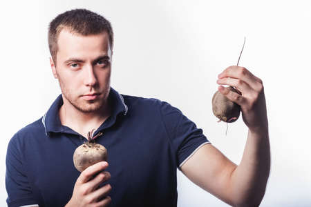 Portrait of an attractive man who tosses vegetables in the studio on a gray background. The concept...