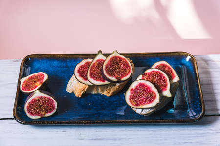 Bruschetta of baguette, cheese and figs are on a plate on the table.