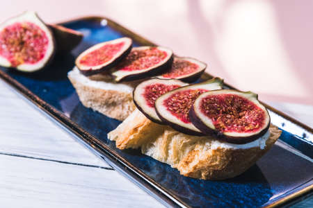 Bruschetta of baguette, cheese and figs are on a plate on the table.