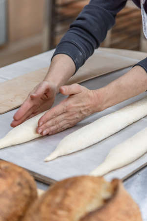 Making craft bread at the bakery. Close-up of a baker and bread, blurred backgroundの写真素材