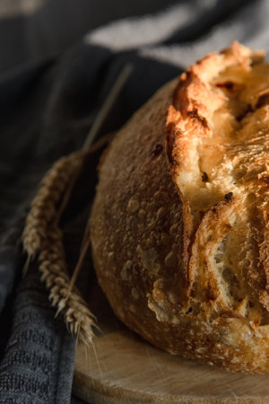 The handcrafted tartin bread lies on a wooden surface next to wheat ears. Farming and home baking...