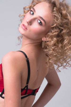 A beautiful woman with make-up and hairstyle in red underwear stands in the studio on a gray background. The concept of fashion photography, clothing and accessoriesの写真素材
