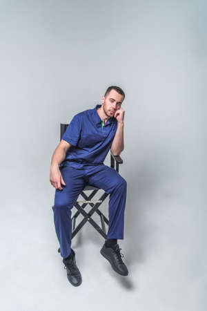 A young man in medical clothes and a robe sits in the studio on a gray background. Medical treatment and healthcare conceptの写真素材