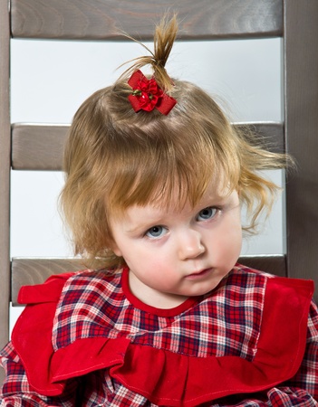 Cute little girl in red dress posing on a chairの写真素材