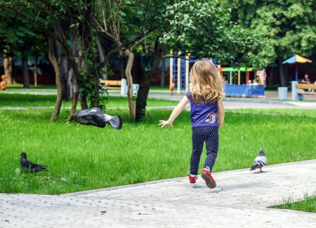 Cute little girl frighting pigeons on playgroundの写真素材