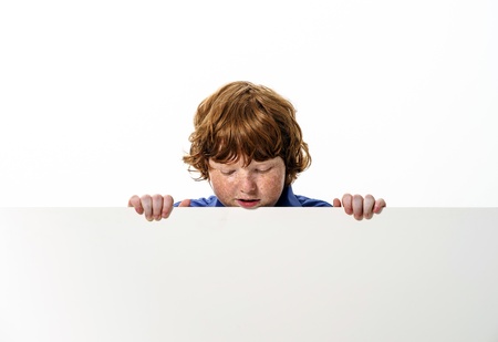 Freckled red-hair boy showing to the white board. Isolated on white background.の写真素材