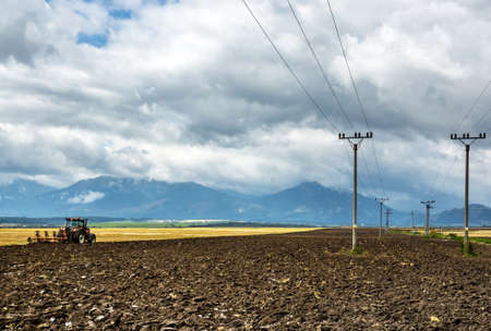 Agrimotor working in fields. Mountains and clouds on backgroundの写真素材