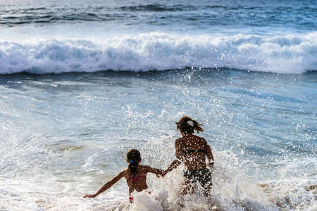 Mother with daughter jumping into waves. Portugal coast.の写真素材