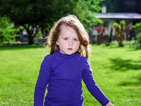 Cute little girl on green grass background near homeの写真素材