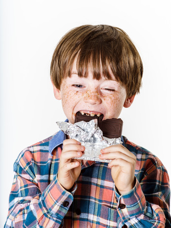 Happy red-haired boy with chocolate bar isolated on whiteの写真素材