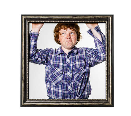 Emotional red-haired boy posing with picture frame isolated on whiteの写真素材