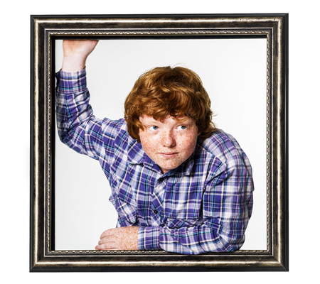 Emotional red-haired boy posing with picture frame isolated on white