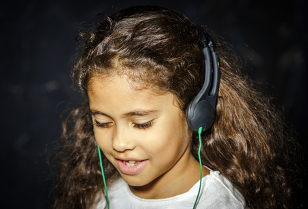 Cute little african-american girl listening music by headphonesの写真素材