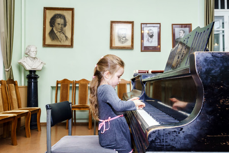 Cute little girl playing grand piano in music schoolの写真素材