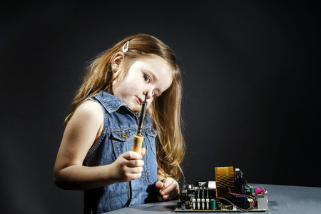 Cute little girl helping father to repair old computer motherboard using soldererの写真素材