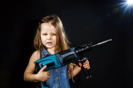 Cute little girl with drilling machine in her hands ready to professional constructing workの写真素材