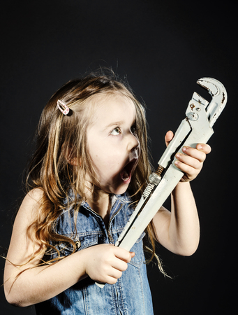 Cute little girl with gas spanner in her hands ready to professional constructing workの写真素材