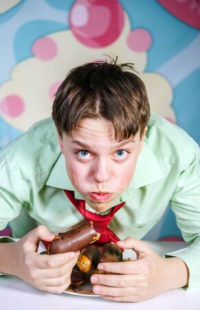 Funny teenage boy eating sweet cakes, hungry and candy manの写真素材