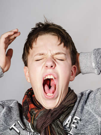 Affective teenage boy portrait in studio isolated on grey backgroundの写真素材