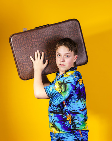 Affective teenage boy with retro suitcase isolated on yellow