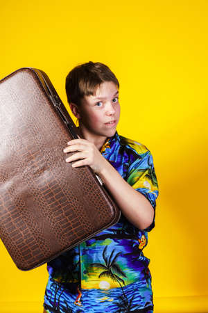 Affective teenage boy with retro suitcase isolated on yellowの写真素材